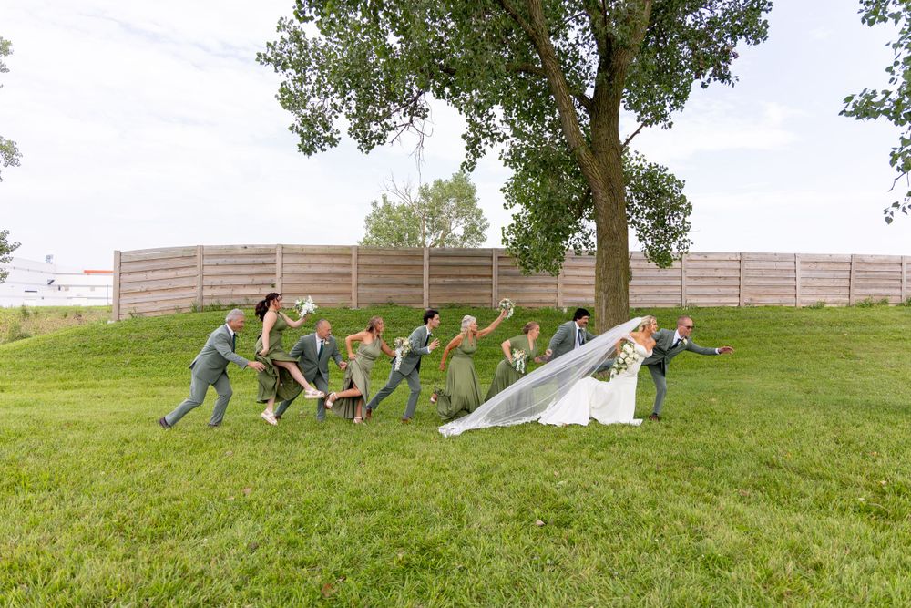 Wedding party celebrates on a grassy hill with dynamic running poses in a playful outdoor moment. Bicentennial Barn, Wedding Photographer.