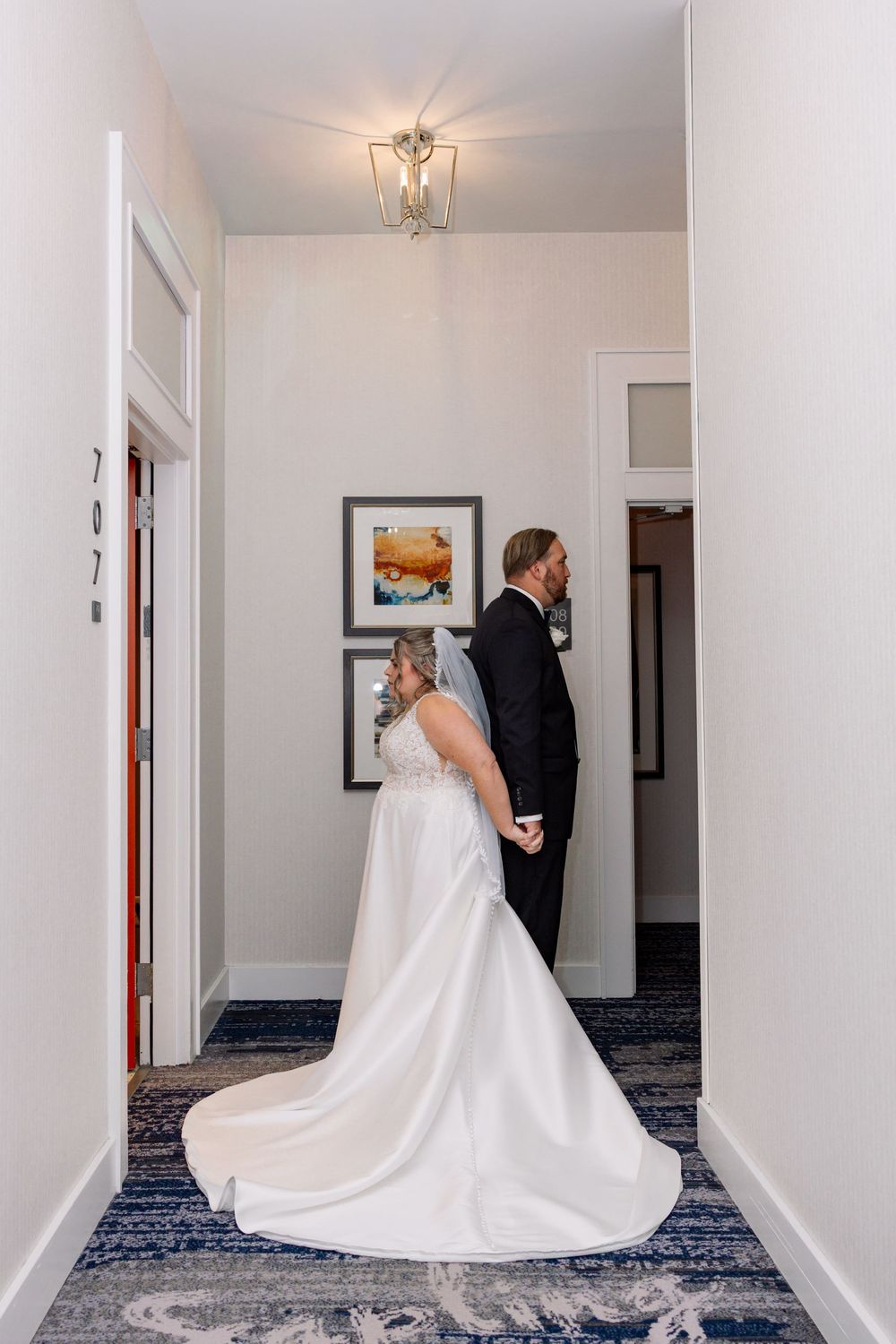 Bride in white gown and groom in black tux share a first look moment in a hotel hallway.