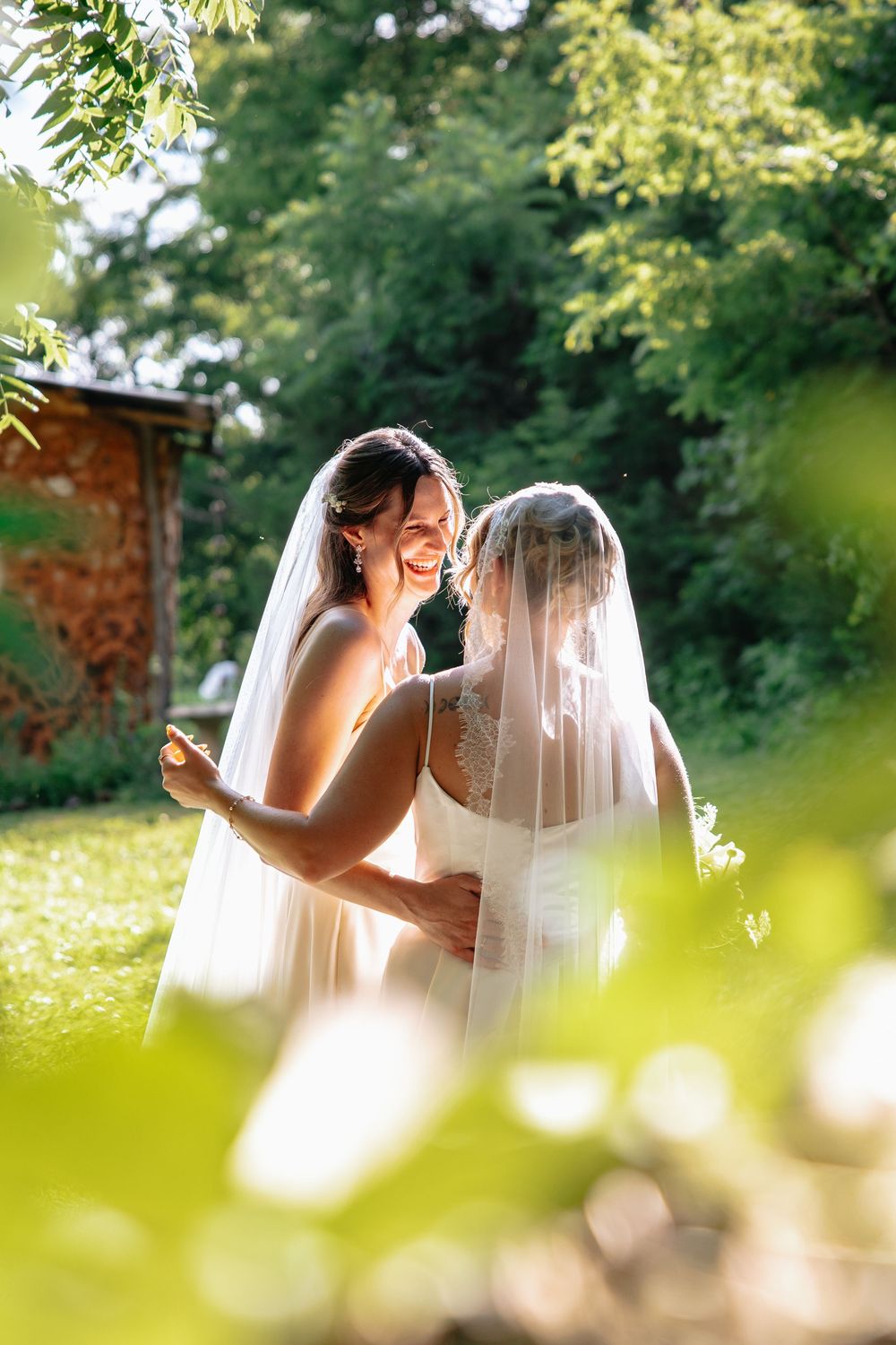 A tender romantic moment captured between newlyweds in a sunlit garden setting with green foliage in the background.