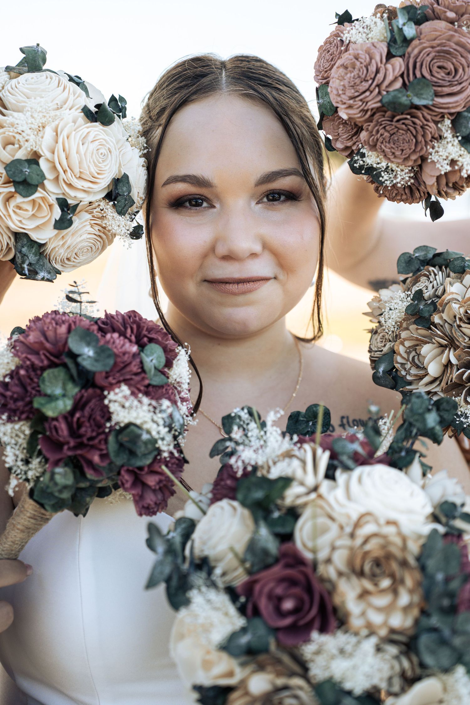 Newlyweds pose together under trees with bride holding pink floral bouquet.