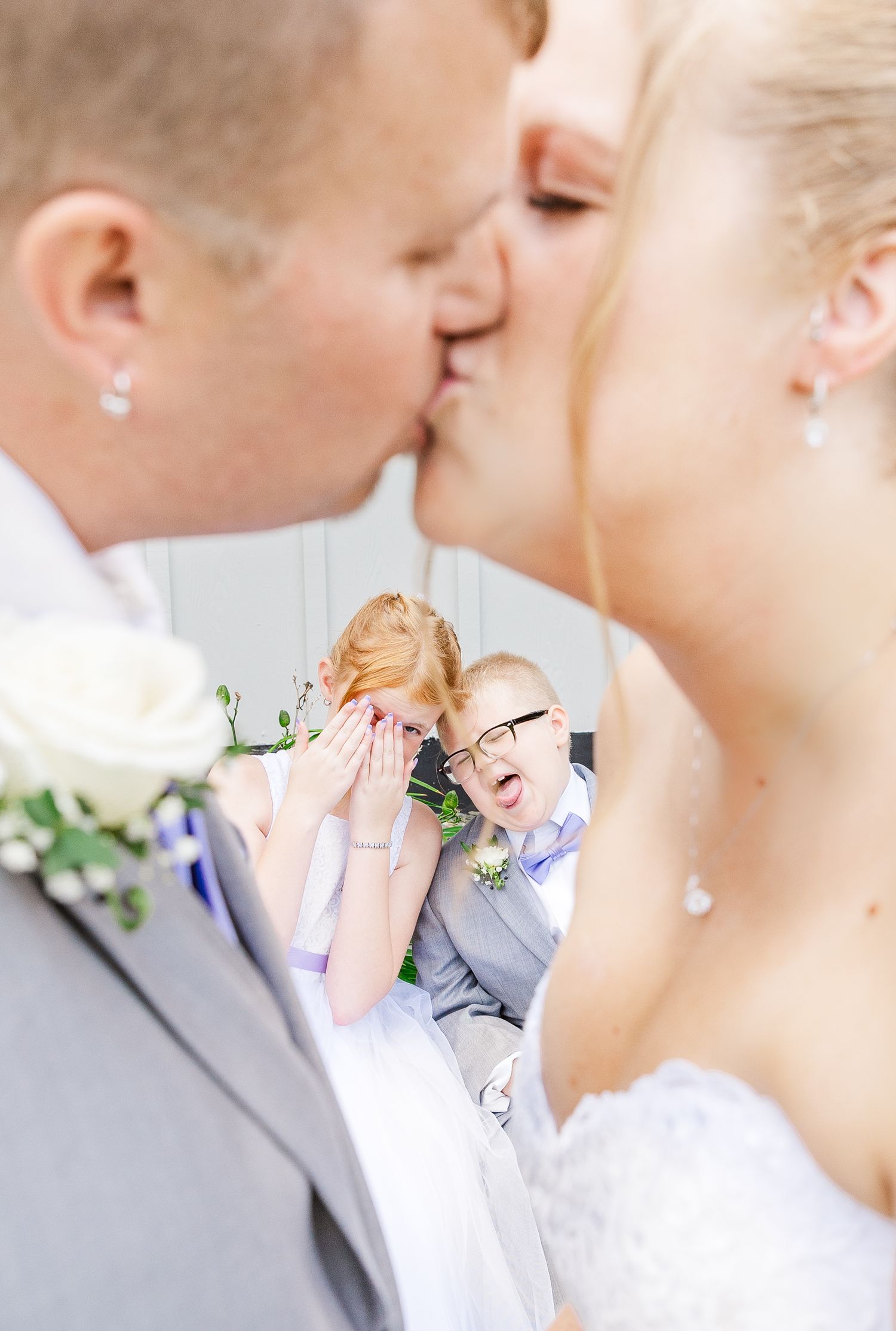 Creative wedding photography moment showing intimate kiss with photobombing reaction in background.