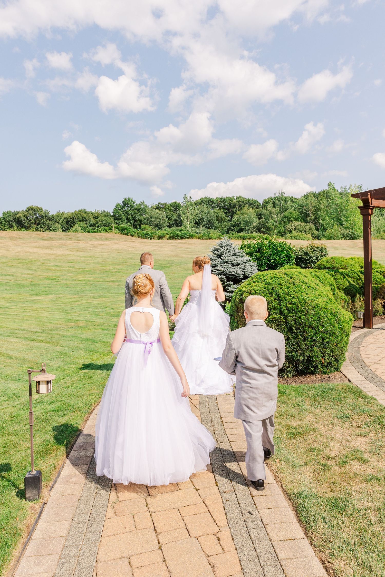 Wedding party walking down a stone path towards a scenic outdoor venue on a sunny day.