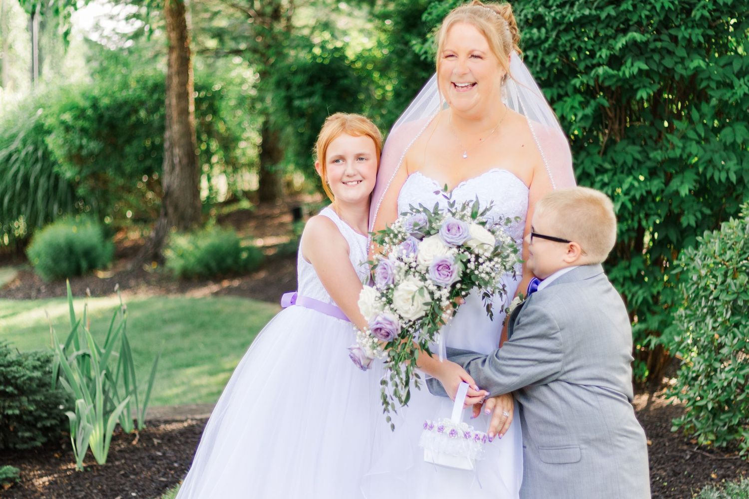 A beautiful outdoor wedding portrait with white and purple floral bouquet against lush greenery.
