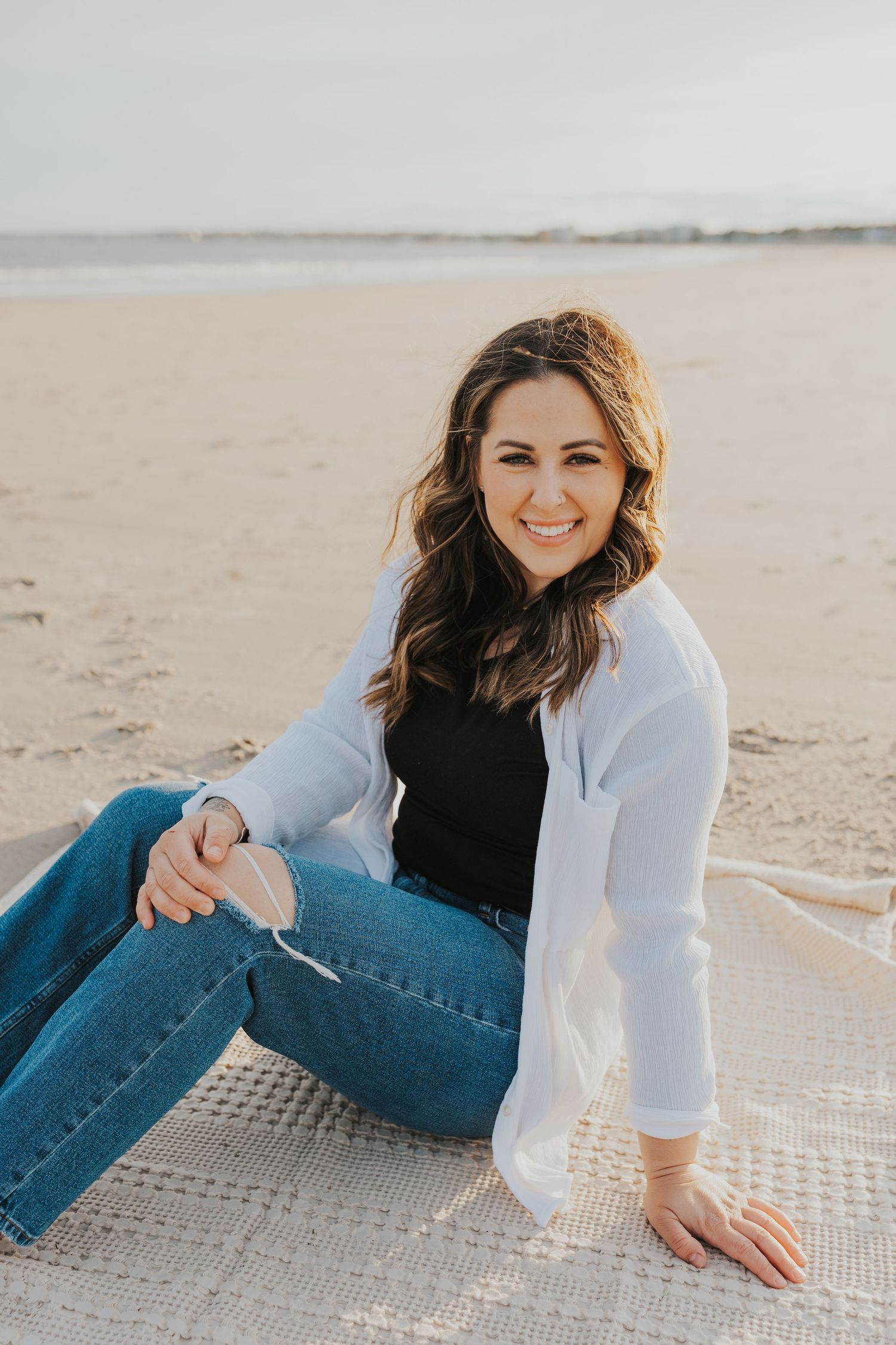 A casual outdoor portrait on a sunny beach with ocean waves in the background.