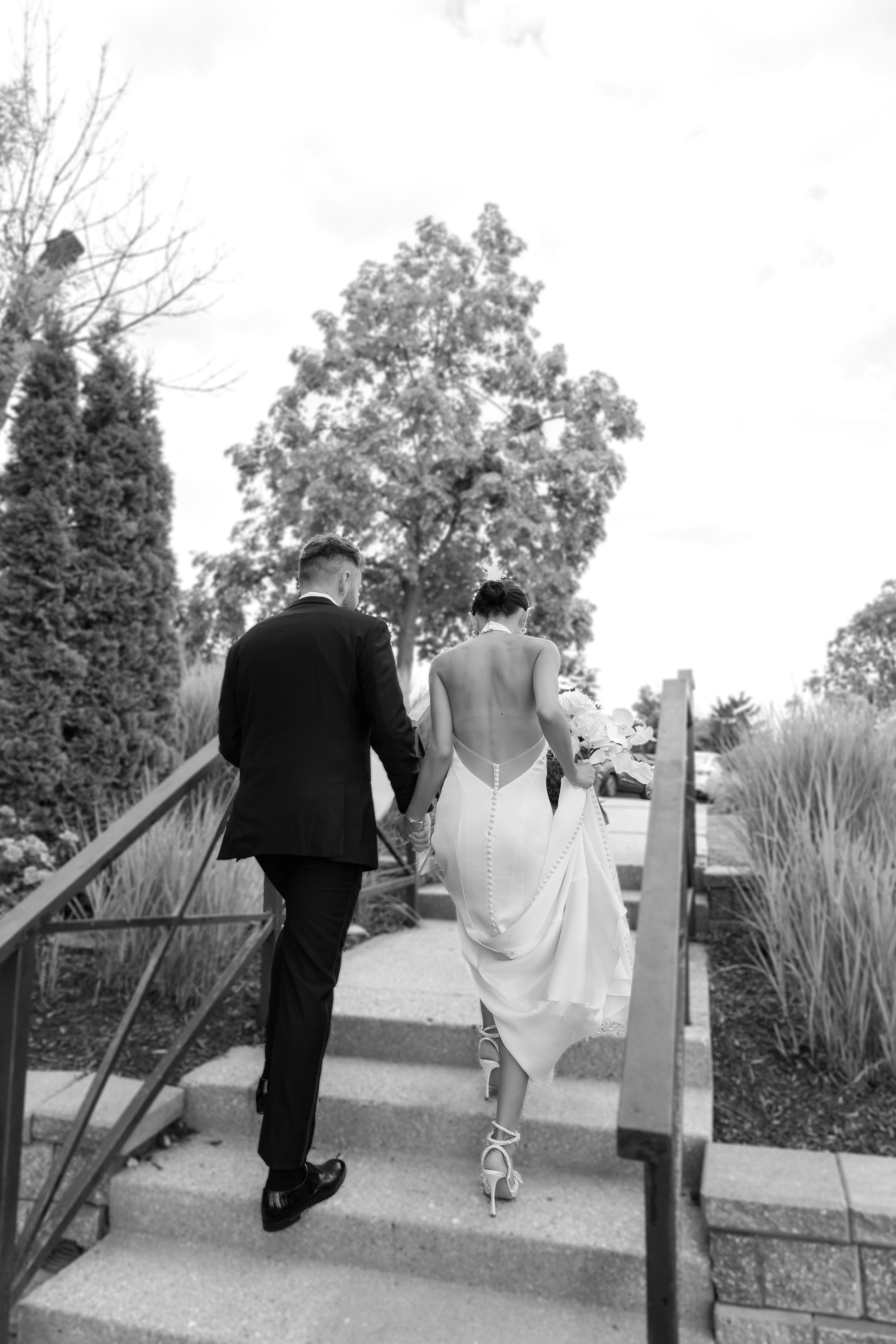 Bride and groom climbing stairs together in an outdoor garden setting.