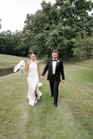 A couple walking hand in hand across a lush green golf course on their wedding day.