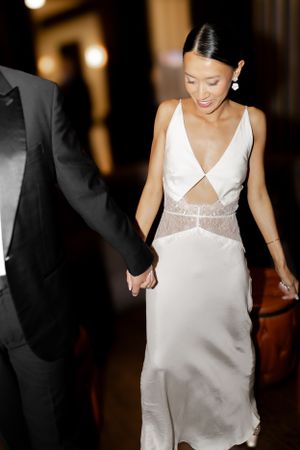 Elegant bride wearing a modern white dress with sheer panels holds hands with her partner.