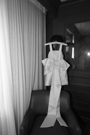 White bridal dress with oversized bow detail displayed on dark chair.
