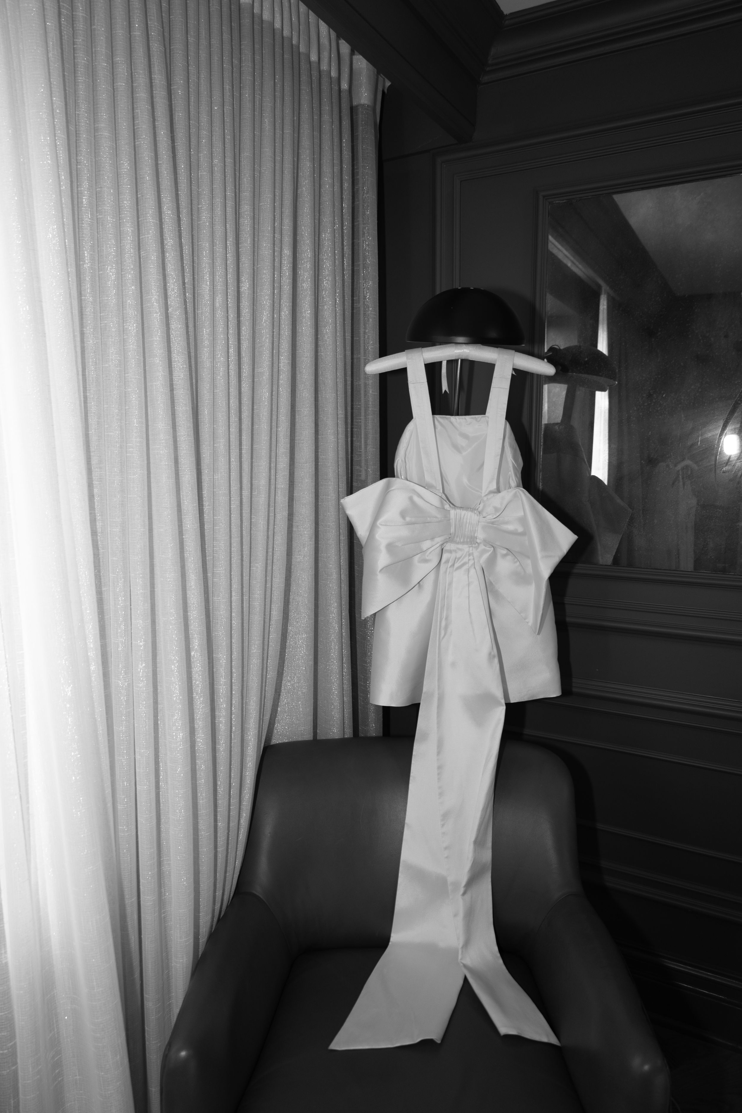 White bridal dress with oversized bow detail displayed on dark chair.