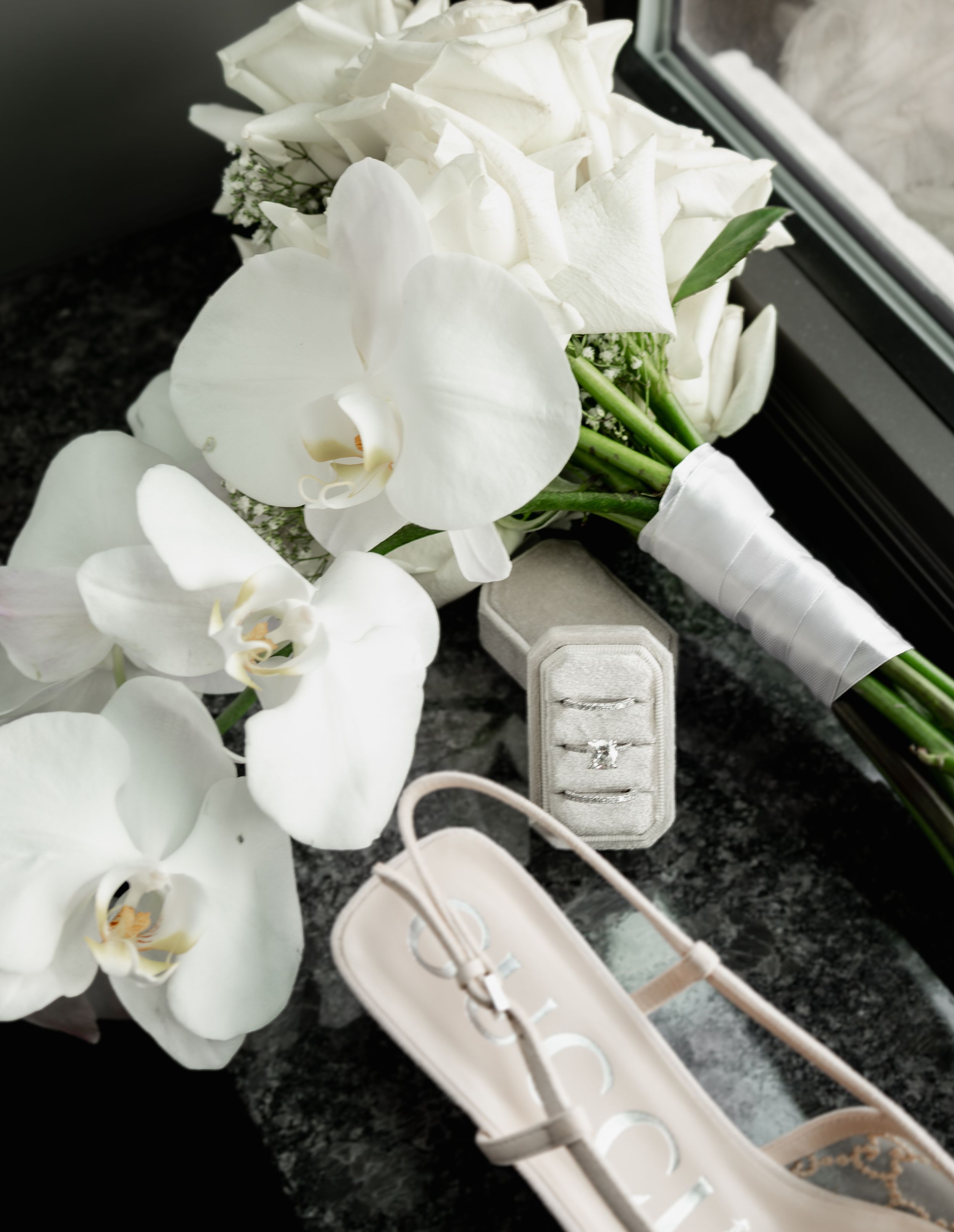Elegant white orchid bouquet with wedding rings and accessories on dark surface.