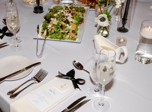 Elegant wedding table setting with white linens, champagne flutes, silverware, menu cards, and a fresh green salad centerpiece.