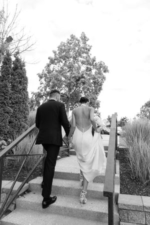Black and white photo of bride and groom holding hands walking up outdoor stairs on their wedding day.