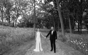 Black and white photo of a bride and groom holding hands on a tree-lined path on their wedding day.
