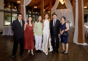 Six elegantly dressed guests posing together at a wedding reception venue with draped white curtains.