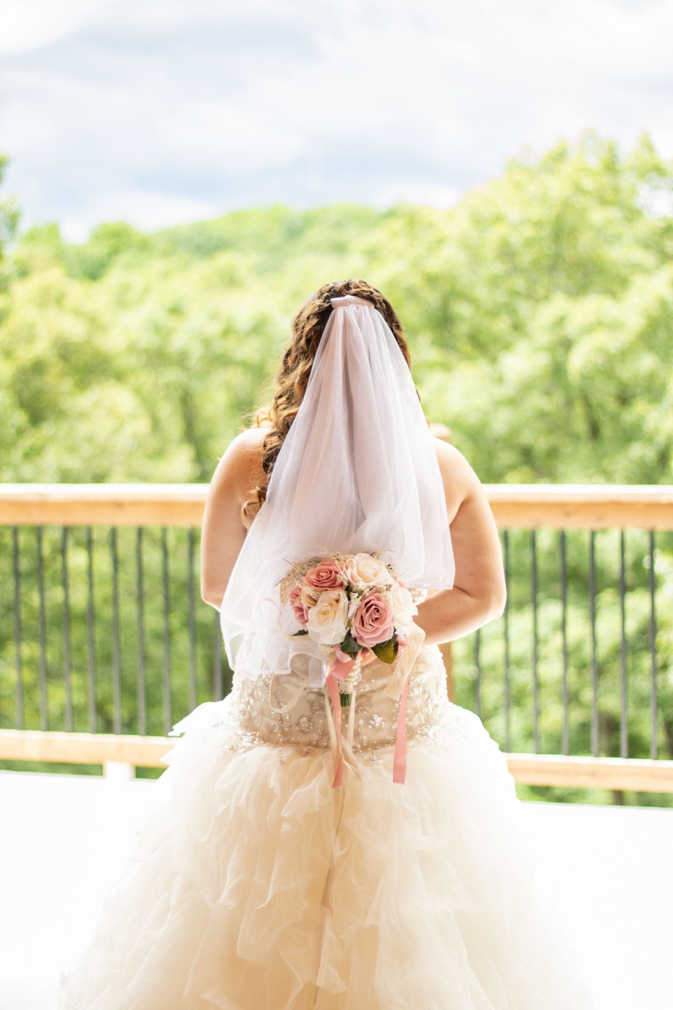 Bride holding her wedding bouquet facing the sky and trees.