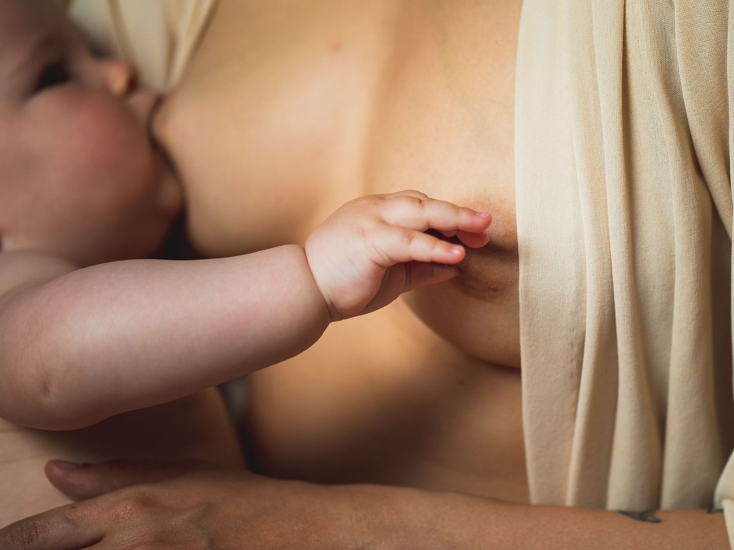 Close-up of a nursing baby's hand resting gently against skin.