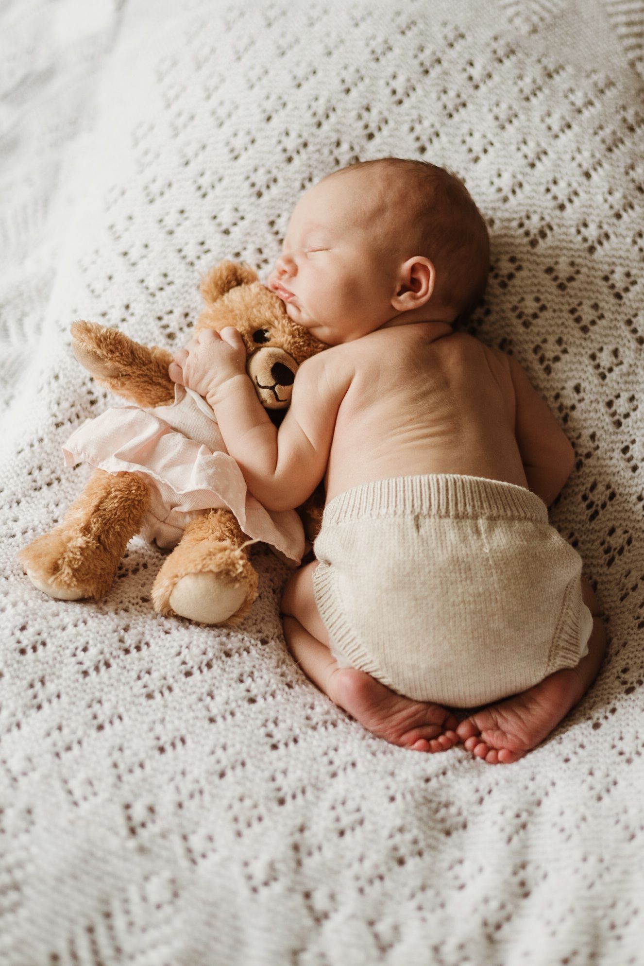 a newborn baby on its tummy asleep cuddling a baby bear