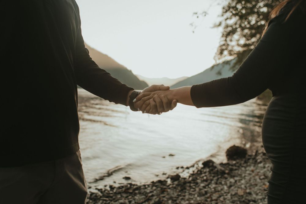 Two people hold hands against a waterfront background in soft lighting.