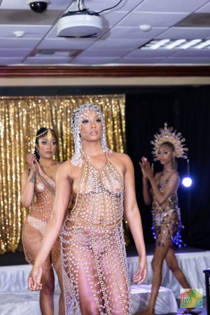 Models present shimmering crystal-adorned costumes against gold curtain backdrop at fashion show.