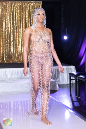 Model showcases dramatic crystal bodysuit with headpiece against gold sequin backdrop.