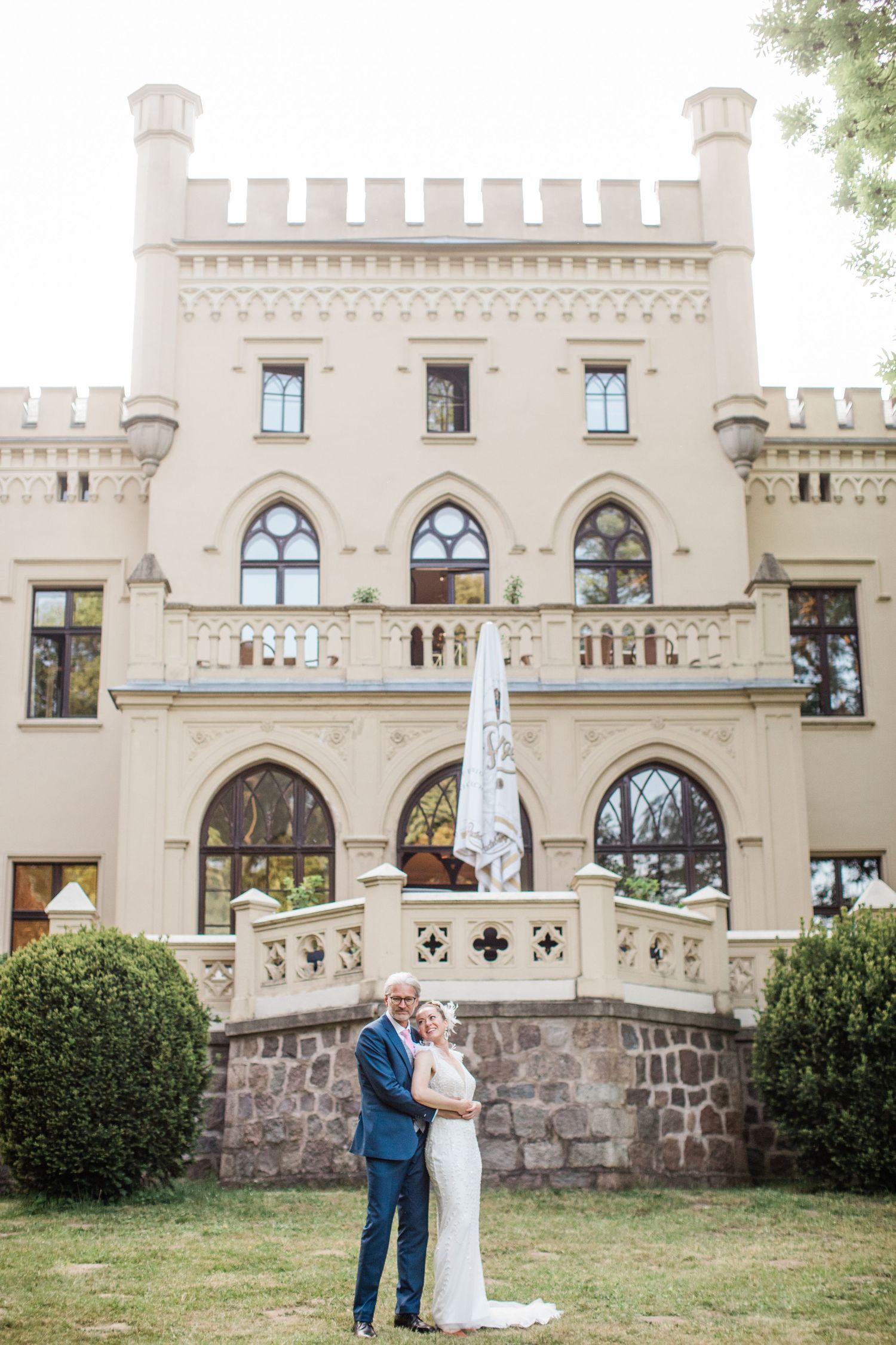 Romantic castle wedding photoshoot on grounds of elegant stone mansion with gothic architectural details and arched windows.