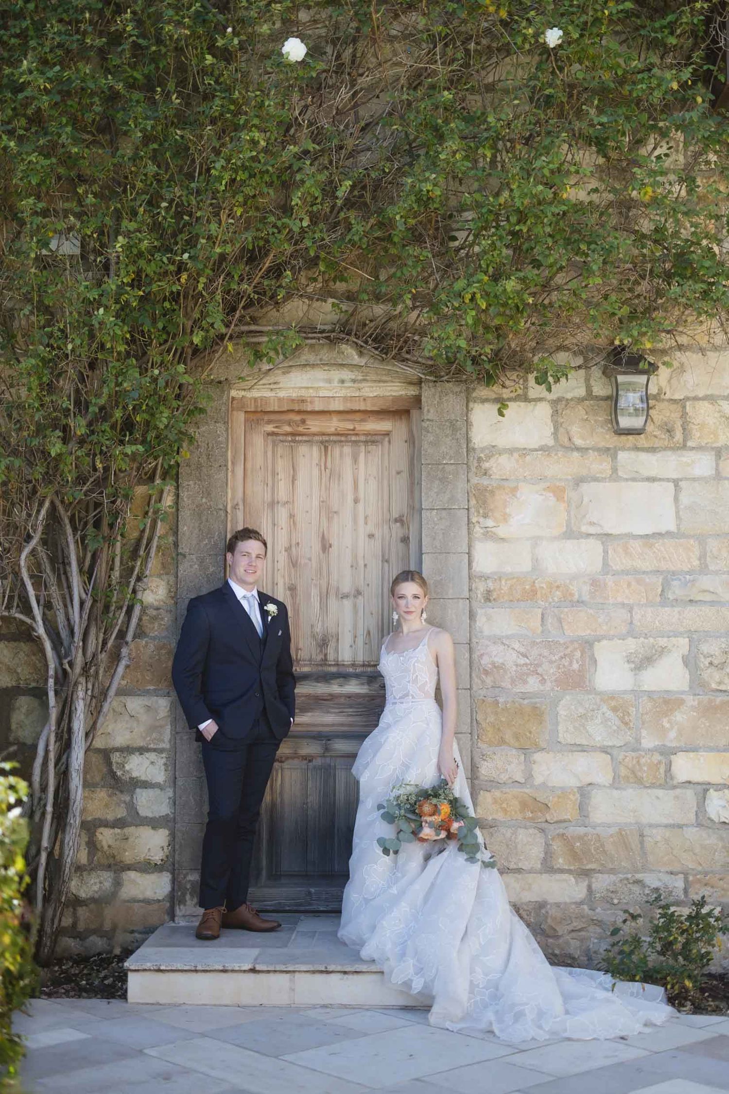 Wedding couple standing in front of rustic wooden door with trailing vines.