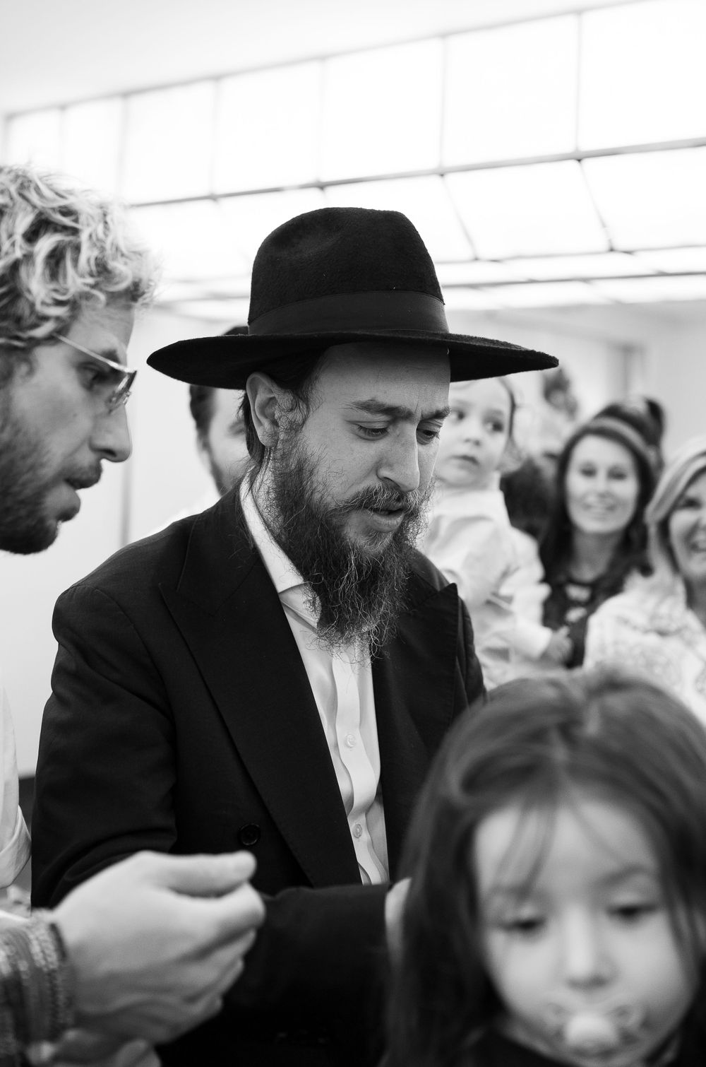 A traditional Jewish ceremony with attendees gathered around a man in a black hat.