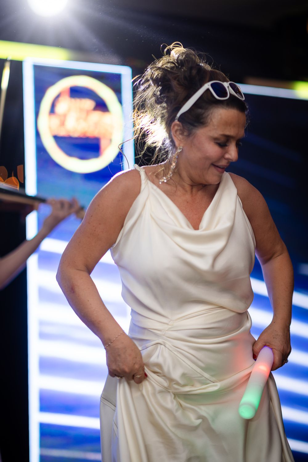 A sequence showing someone in a white dress playfully interacting with a balloon on a stage with neon lights.