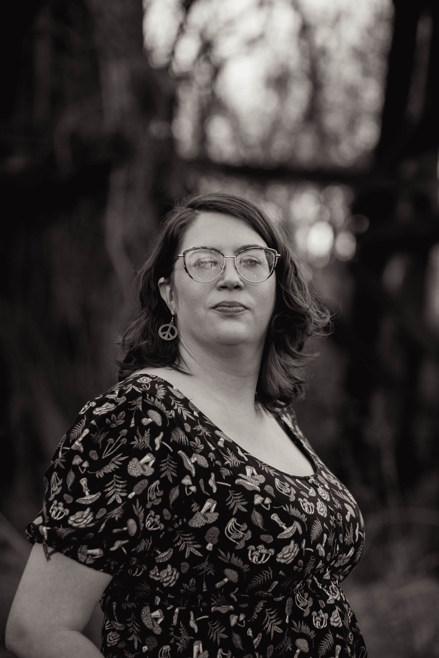 Artistic black and white portrait of person in glasses against blurred forest background.