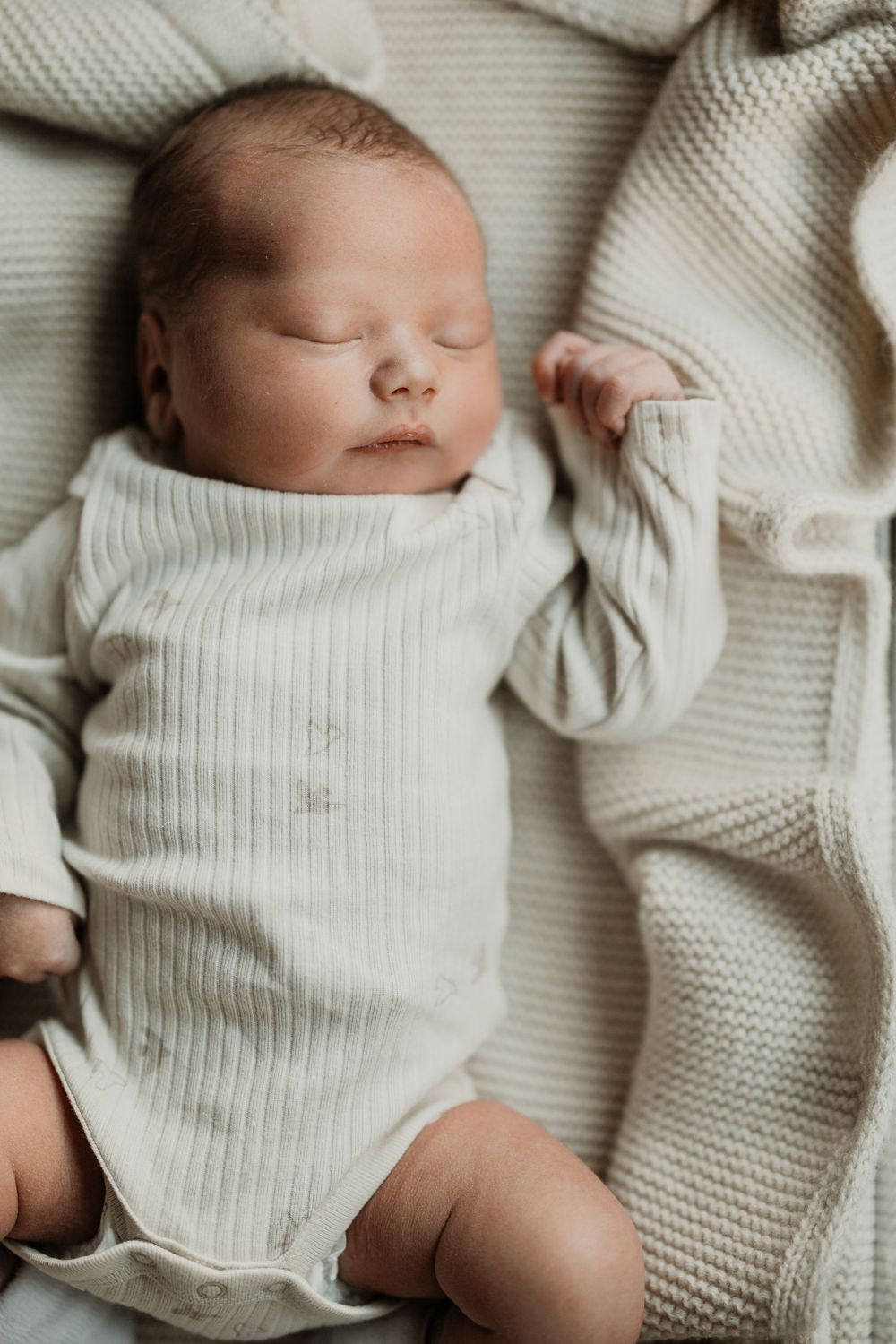 Newborn baby wearing soft white knit clothing while sleeping peacefully.