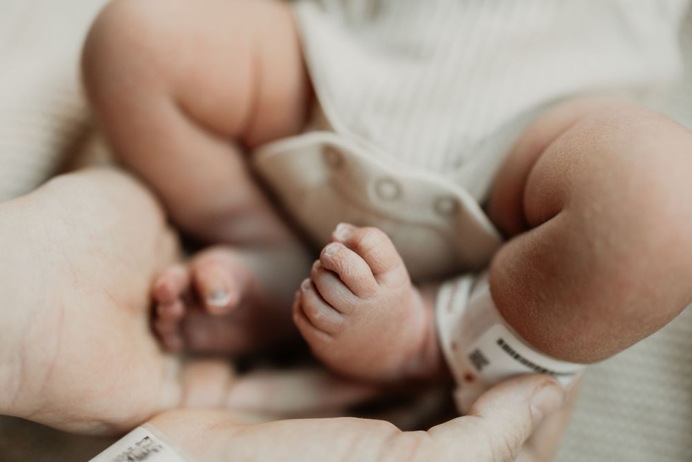 Tiny newborn feet and hands resting on white textured blanket.