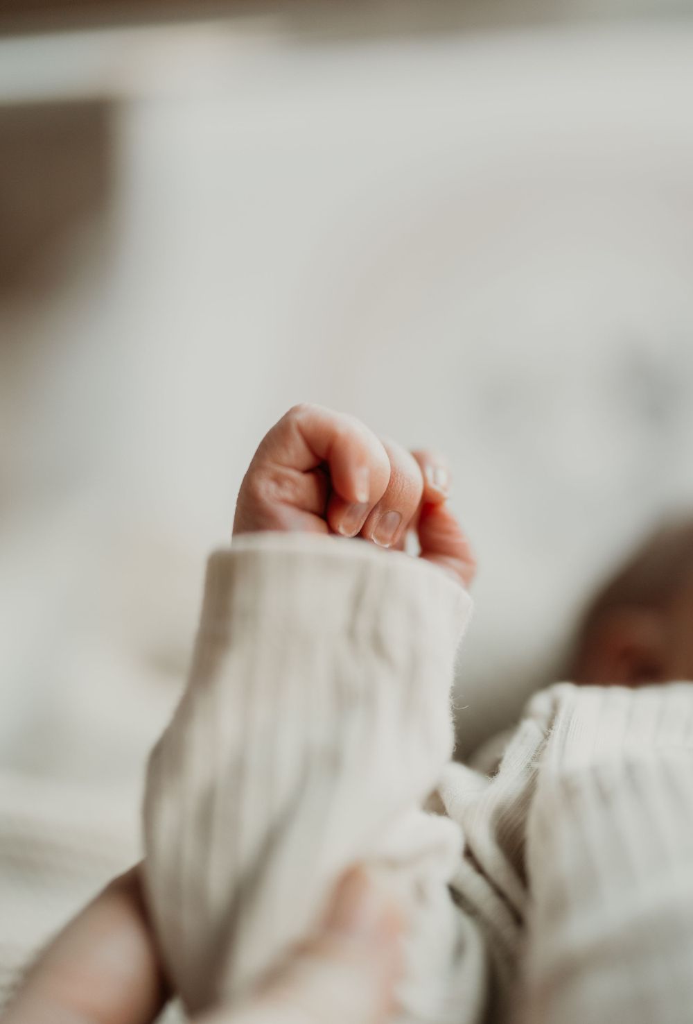 Close-up of small baby hands grasping white knitted fabric.