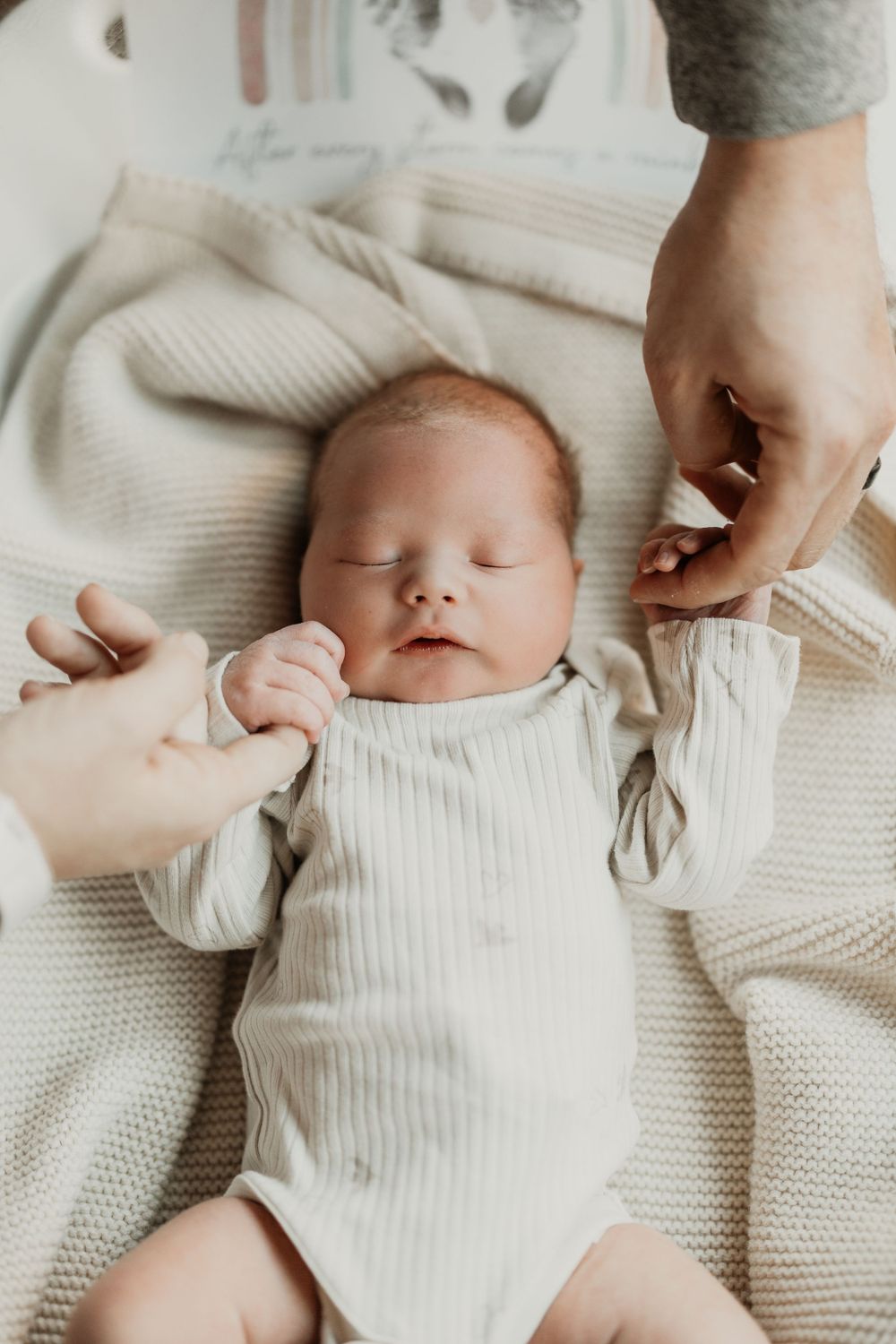 Peaceful newborn in white ribbed onesie lying on textured cream blanket.