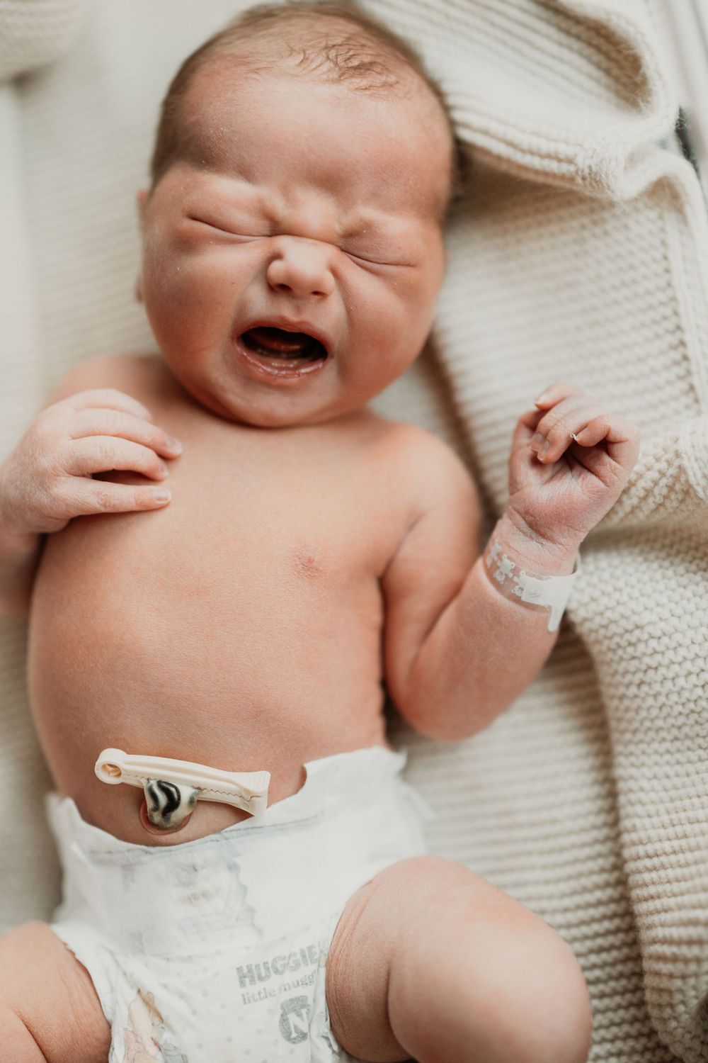 Newborn baby stretching and yawning while wearing white knit clothing.