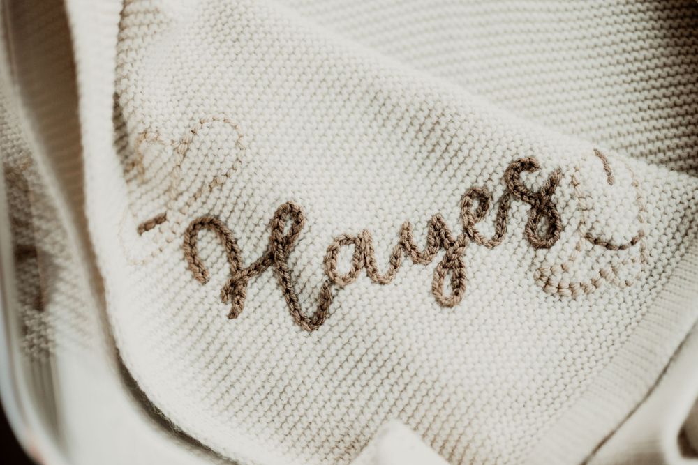 Embroidered 'prayers' text in brown thread on white fabric.
