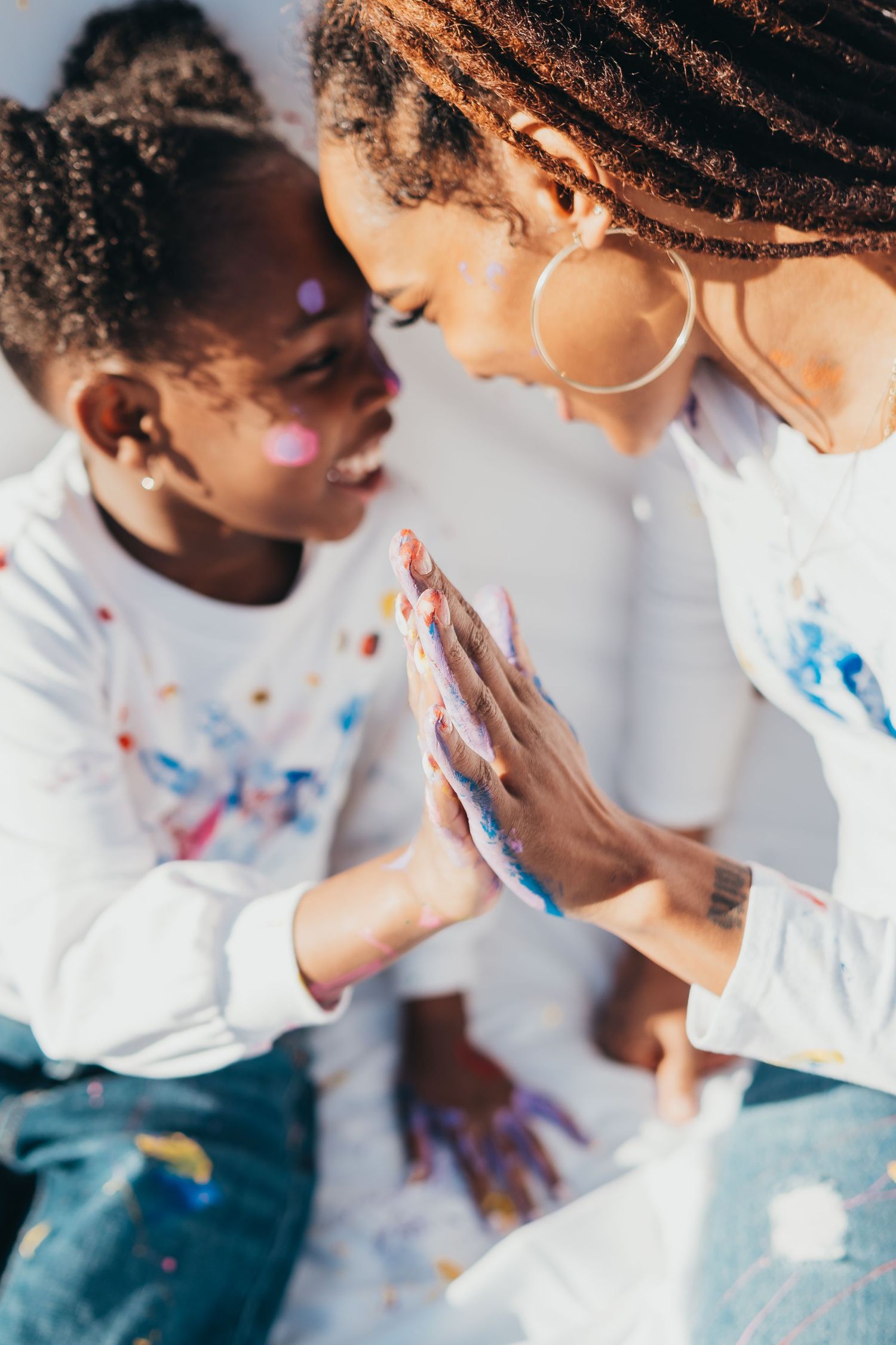 Two people in white shirts with paint-splattered hands lean close together during a creative moment.