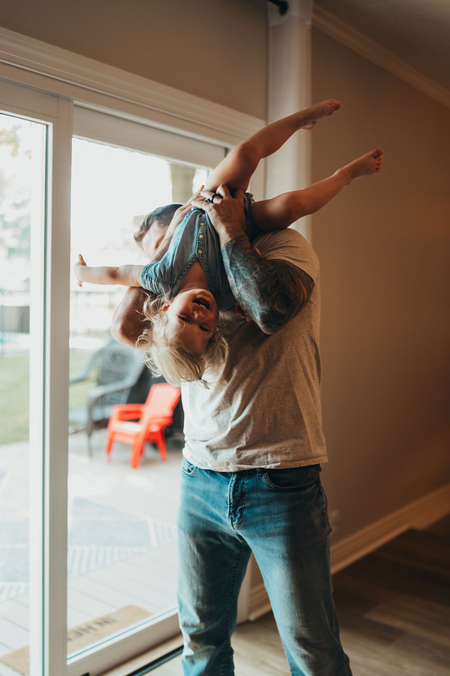 Playful sequence showing a parent lifting and swinging a child in front of large windows.