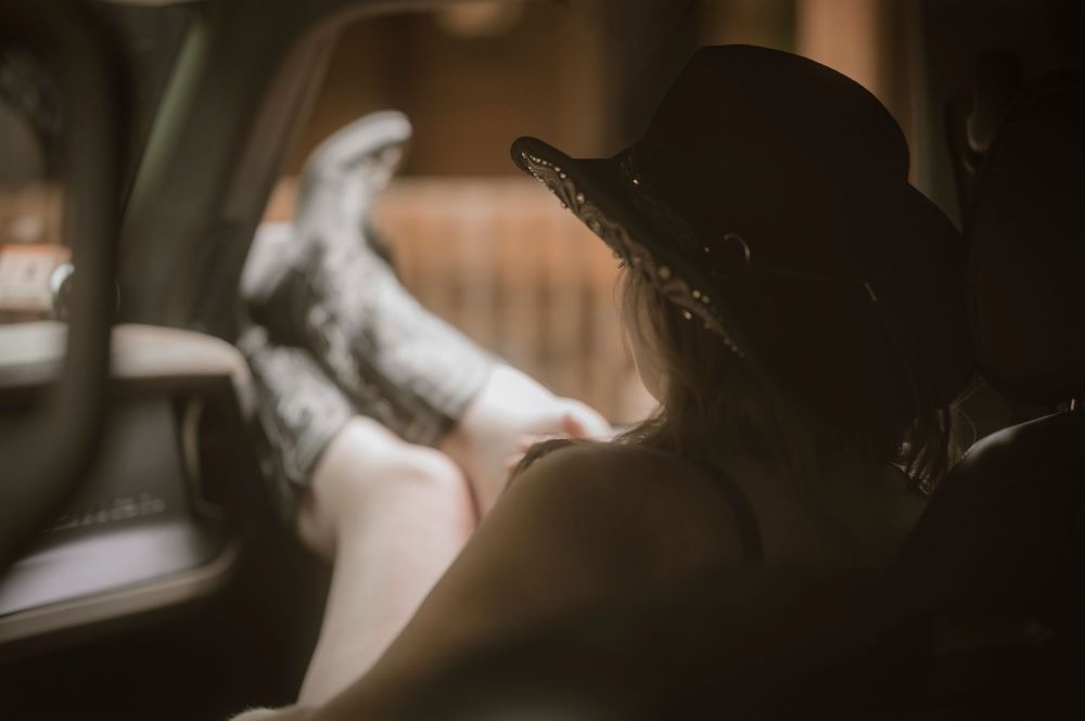 Person in a cowboy hat relaxing in a vintage car with feet up on the dashboard, captured in warm sepia tones.
