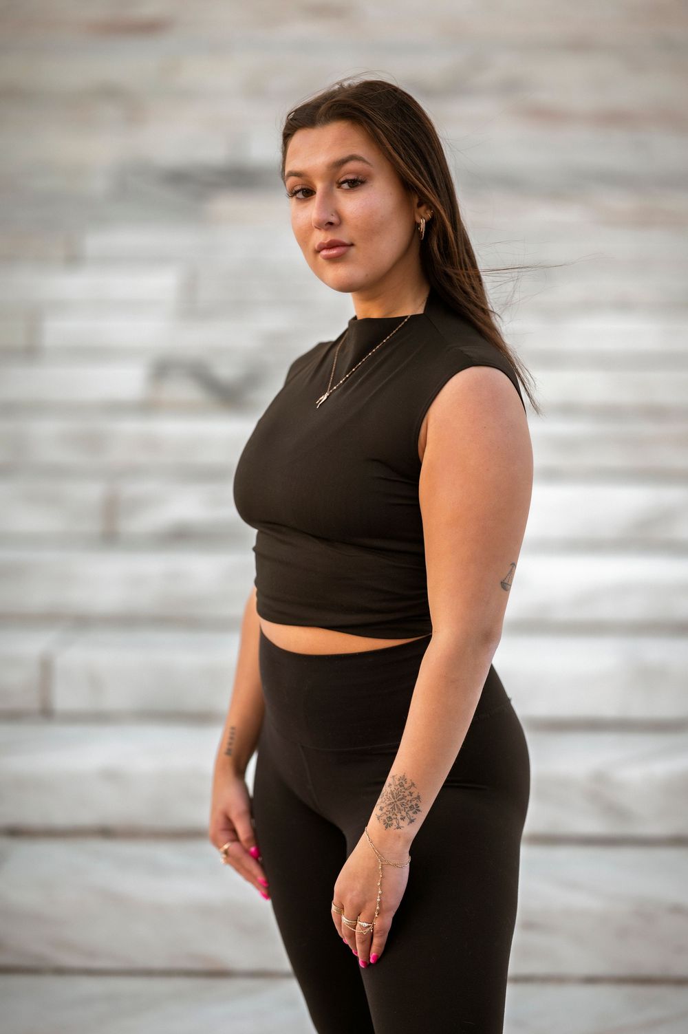 Athletic figure in a black crop top and leggings poses confidently on concrete steps during a portrait session.