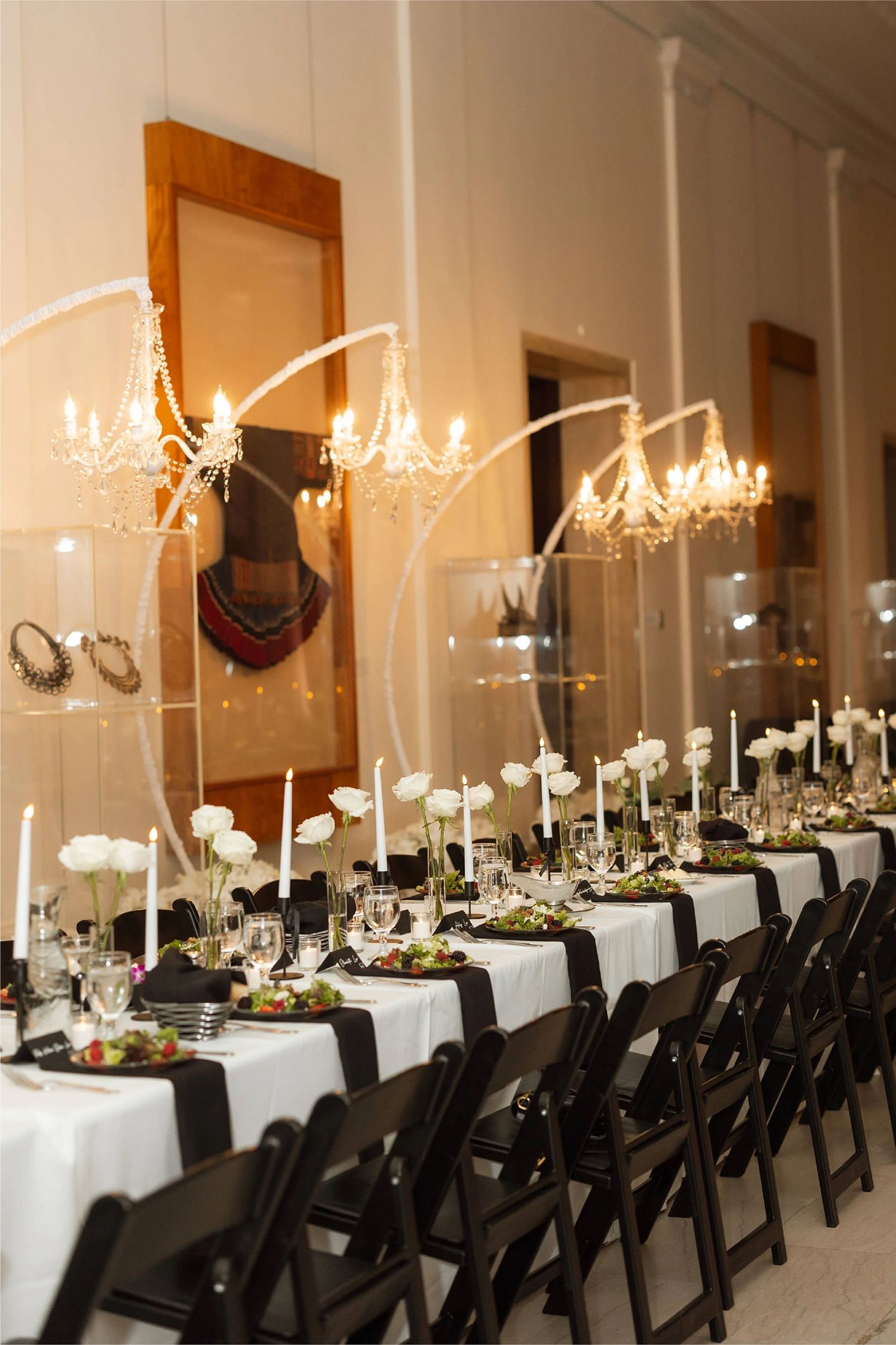An elegant wedding reception table with white linens and hanging crystal chandeliers.