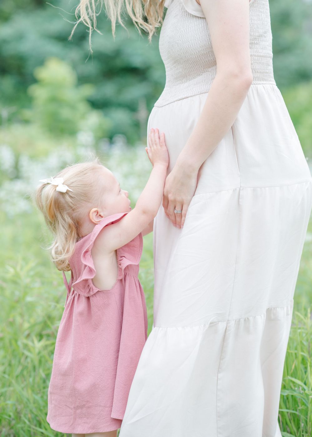 Toddler in pink dress holding mother’s baby bump during outdoor maternity session in Normal, Illinois by Julie Loy Photography