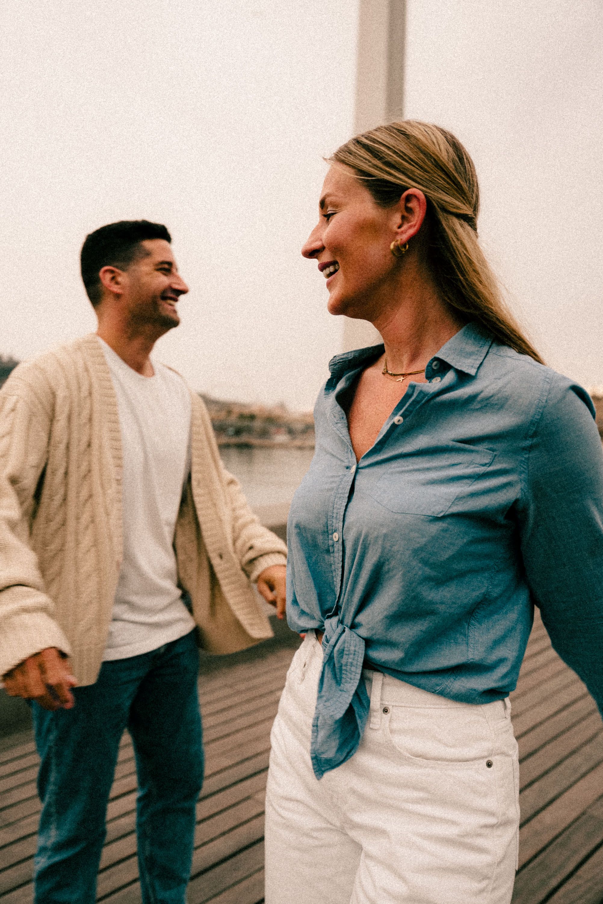 A couple shares a joyful moment while walking on a wooden pier in casual attire.