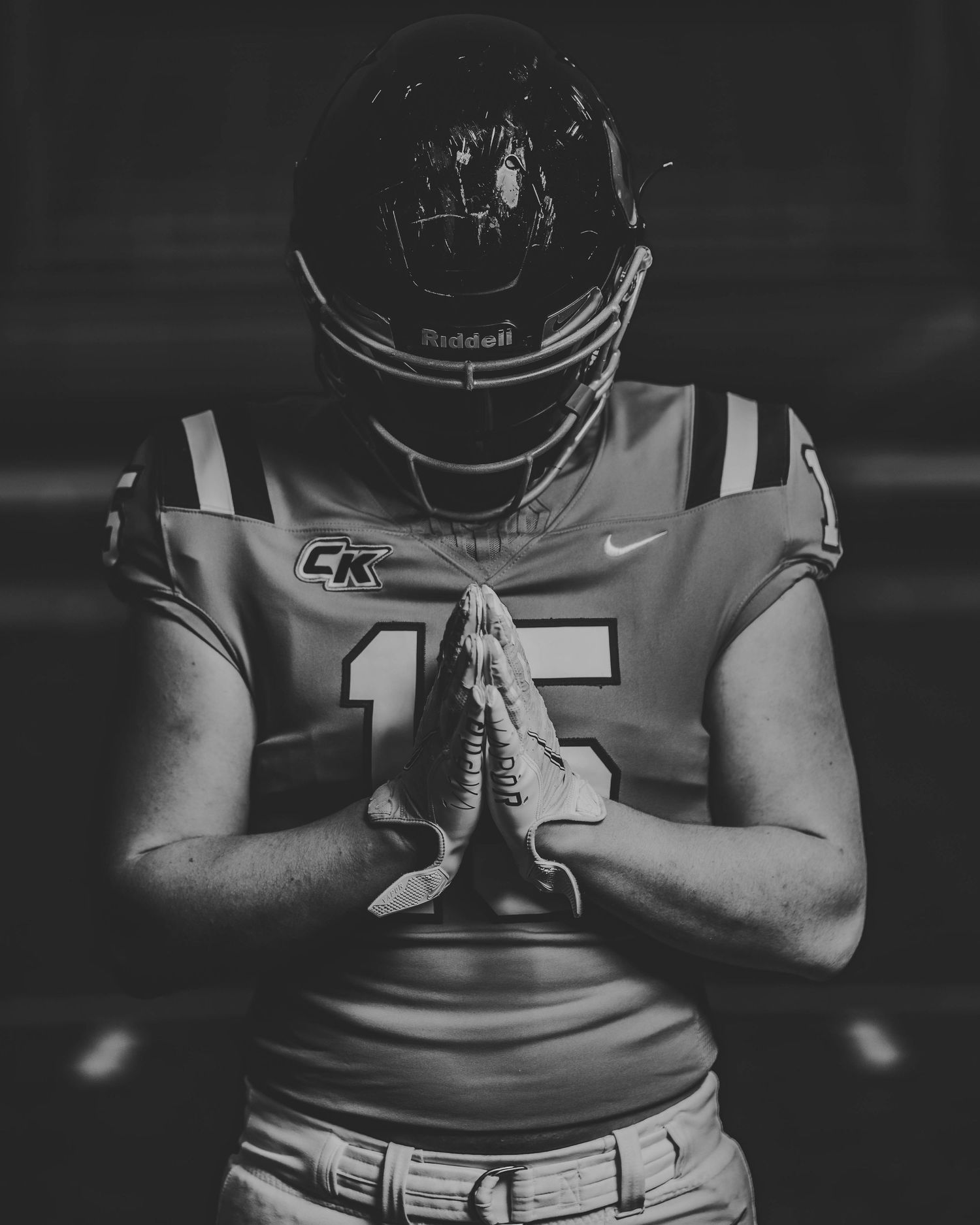 Dramatic black and white portrait of football player in uniform praying with helmet on.
