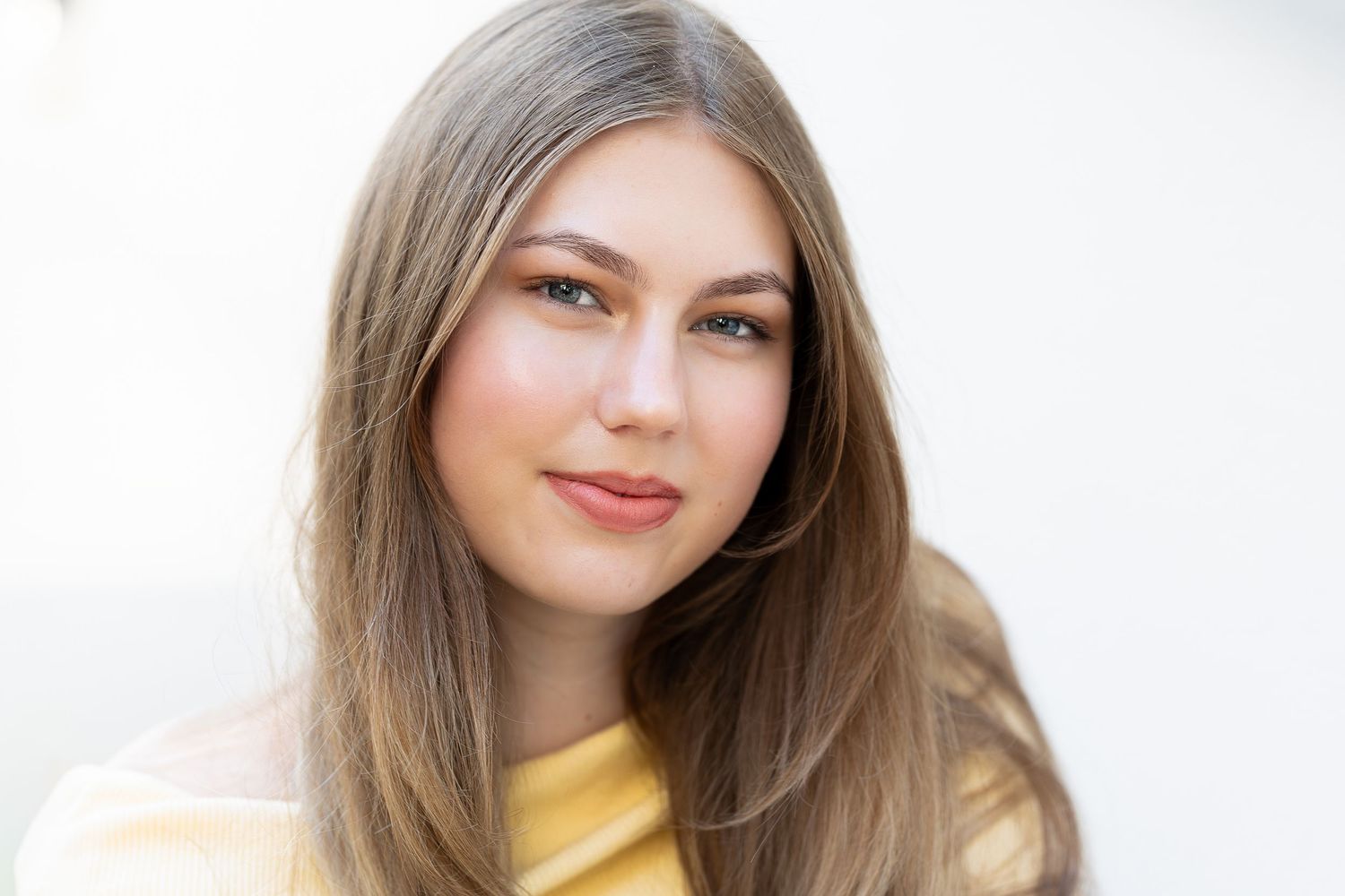 A woman with long brown hair wearing a yellow top smiles warmly at the camera.