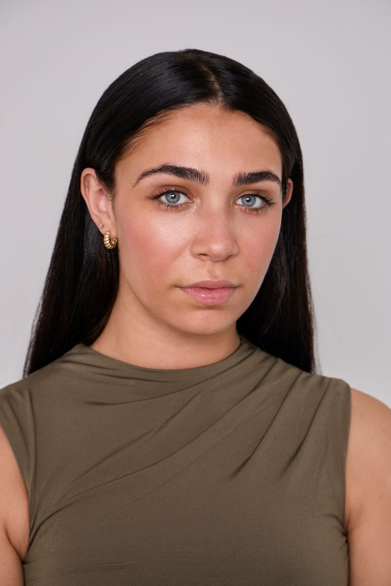Fashion portrait in olive sleeveless top against neutral grey backdrop.