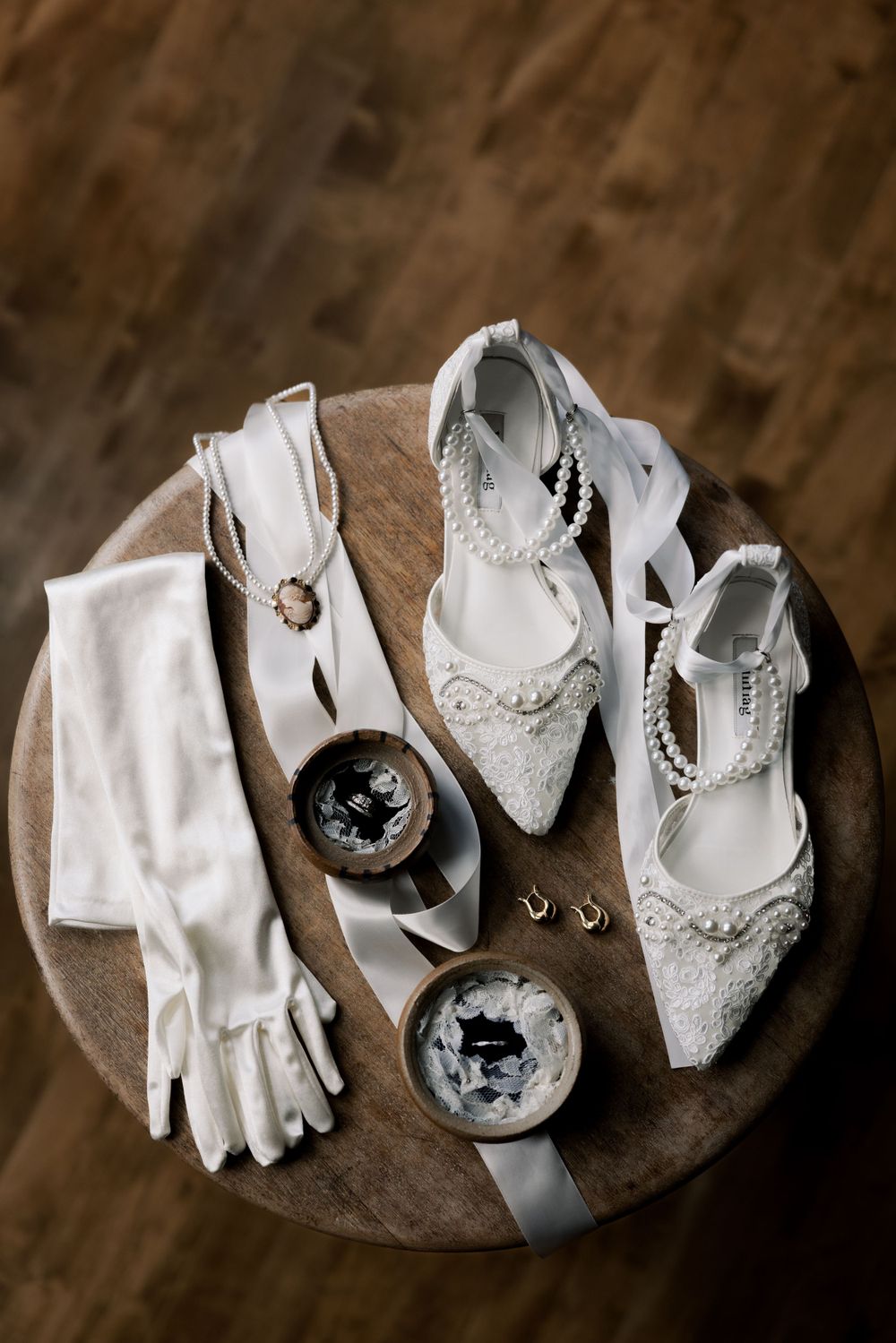Elegant white lace bridal shoes with gloves and decorative boxes arranged on wooden surface.
