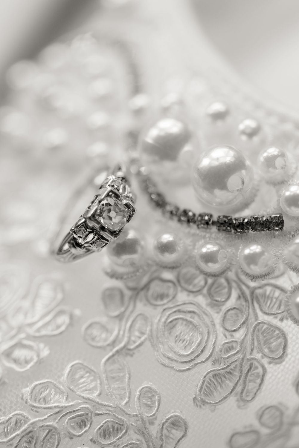 Close-up of intricate pearl and lace details with diamond ring in black and white.