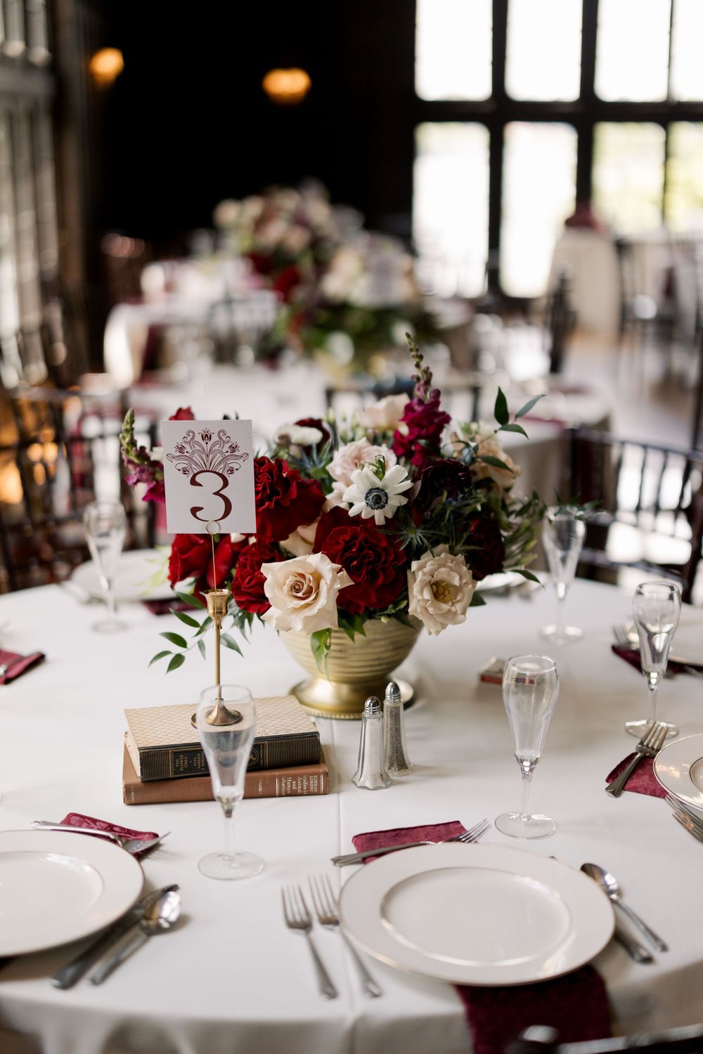 Elegant wedding table setting with burgundy and cream floral centerpiece and table number.