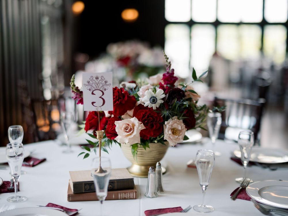 Wedding reception table decorated with burgundy and blush roses in gold vase.