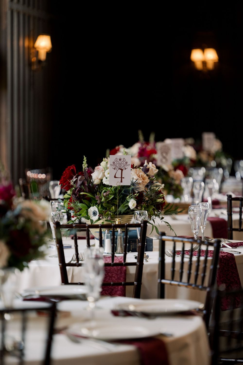 Wedding reception venue with dark wood chairs and burgundy floral centerpieces.